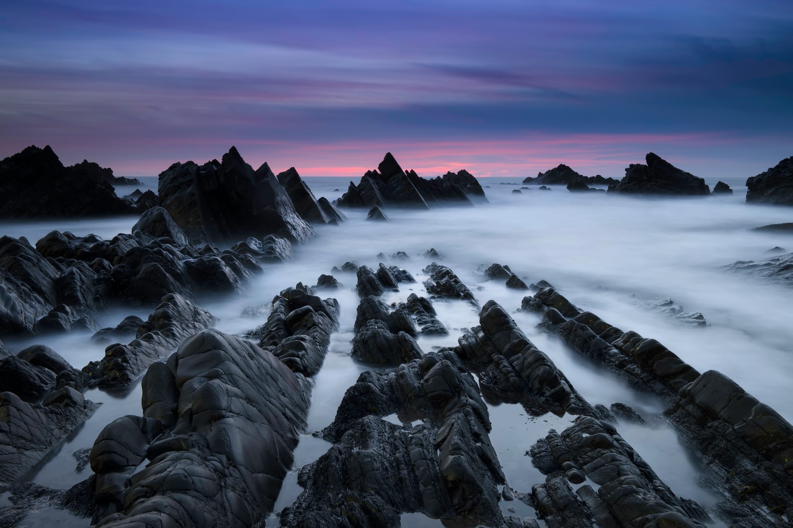 Uma fotografia de longa exposição de uma praia rochosa ao pôr do sol (atlantic coast, costa rochosa, enevoado, névoa, anoitecer)