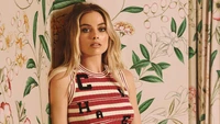 Margot Robbie con un elegante atuendo a rayas rojas y blancas contra un fondo floral.