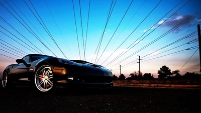 Eleganter Chevrolet Corvette vor einem lebhaften Sonnenuntergangshimmel, der seine Leichtmetallräder und dynamische Haltung zeigt.