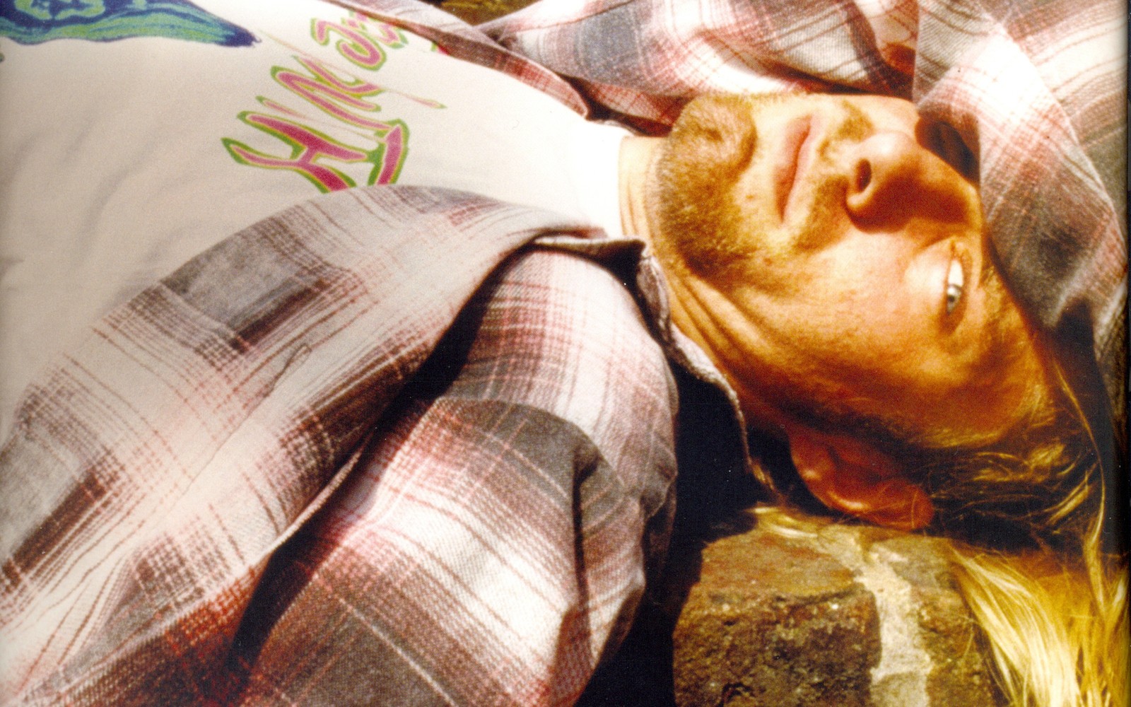 Arafed man laying on a rock with a plaid shirt on (human, nirvana, grunge, music, punk fashion)