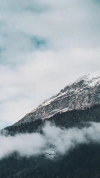 Majestätischer Berg unter einem bewölkten Himmel mit einem vorbeifliegenden Flugzeug