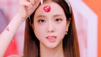 Jisoo do BLACKPINK segura brincando uma cereja na testa, mostrando seu charme e estilo em um ambiente vibrante e colorido.