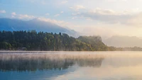 Paisaje de lago sereno con montañas brumosas y bosques exuberantes