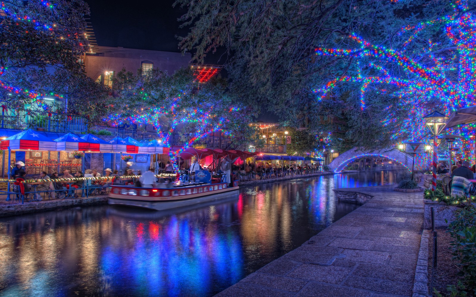 A view of a boat is parked on the river with christmas lights (christmas day, christmas lights, night, waterway, reflection)