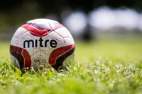 Balón de fútbol Mitre descansando sobre hierba verde.