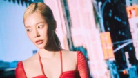 Sunny de Girls' Generation dans une tenue rouge frappante, sur fond d'un décor urbain vibrant, dégageant confiance et style.