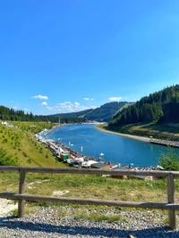 Paisagem de fiorde serena com um curso de água azul sinuoso cercado por montanhas exuberantes e encostas arborizadas.