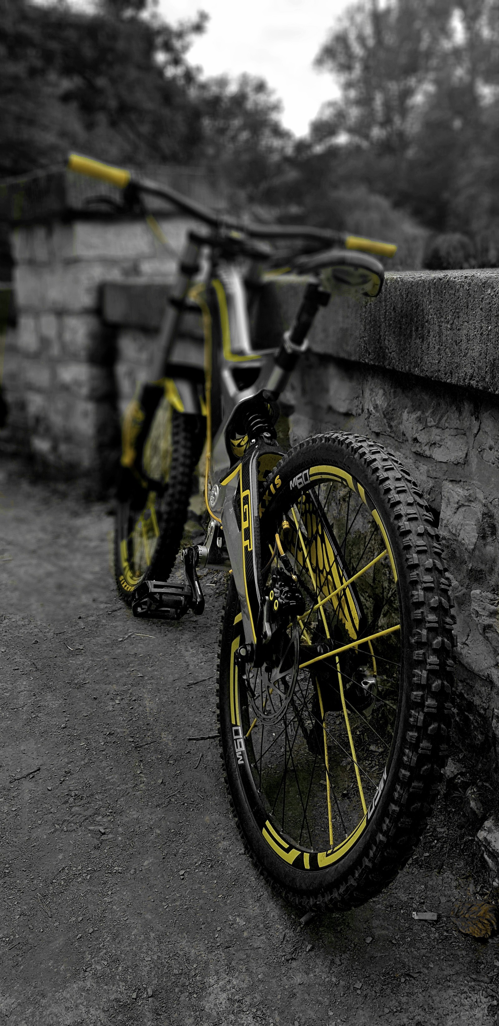 Un vélo jaune appuyé contre un mur en pierre sur un fond noir et blanc (vélo, cycle)