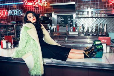 Charli XCX showcases bold fashion in a diner setting, lounging on a counter in a vibrant fur coat and striking platform shoes.