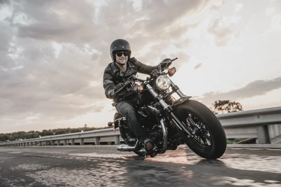 A rider on a custom Harley Davidson motorcycle cruising along an open road at sunset.