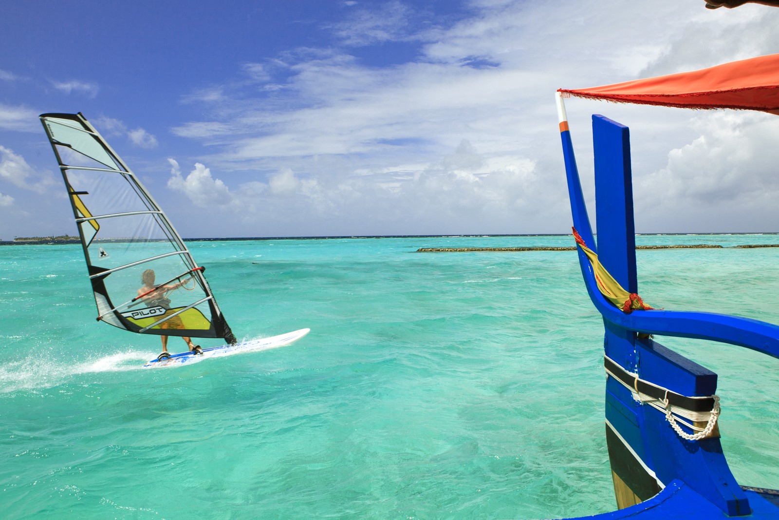 There is a man riding a sail board in the ocean (windsurfing, surfing, sea, wind, sail)