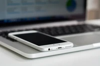 Smartphone descansando sobre un Apple MacBook Pro, mostrando un elegante diseño tecnológico en blanco y plata.