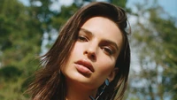 Emily Ratajkowski with flowing hair and striking features against a natural background.