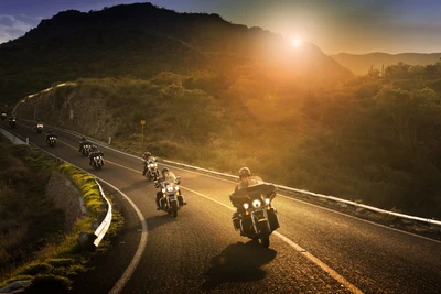 Motociclistas en motocicletas Harley-Davidson recorriendo una carretera montañosa escénica al atardecer.