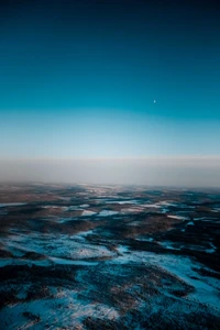 Winterlandschaft: Luftaufnahme von schneebedecktem Terrain unter einem nebligen blauen Himmel