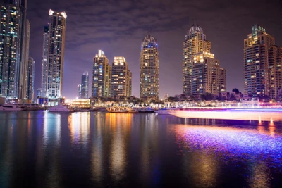 Rascacielos iluminados y reflejos en las serenas aguas de Dubai Marina por la noche, mostrando la vibrante metrópoli de los Emiratos Árabes Unidos.