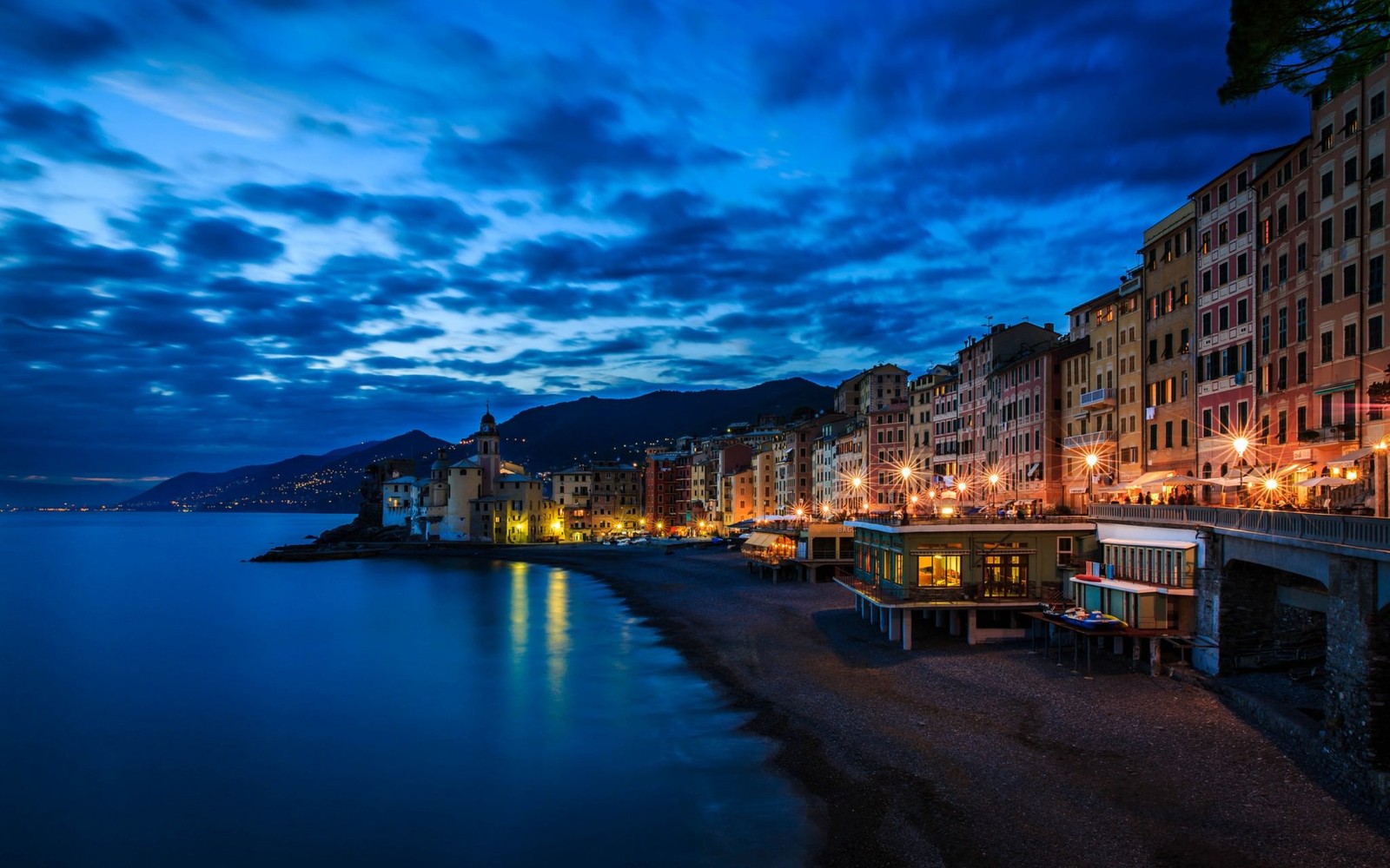 Vista de uma praia com um píer e edifícios à noite (água, noite, reflexo, anoitecer, iluminação)