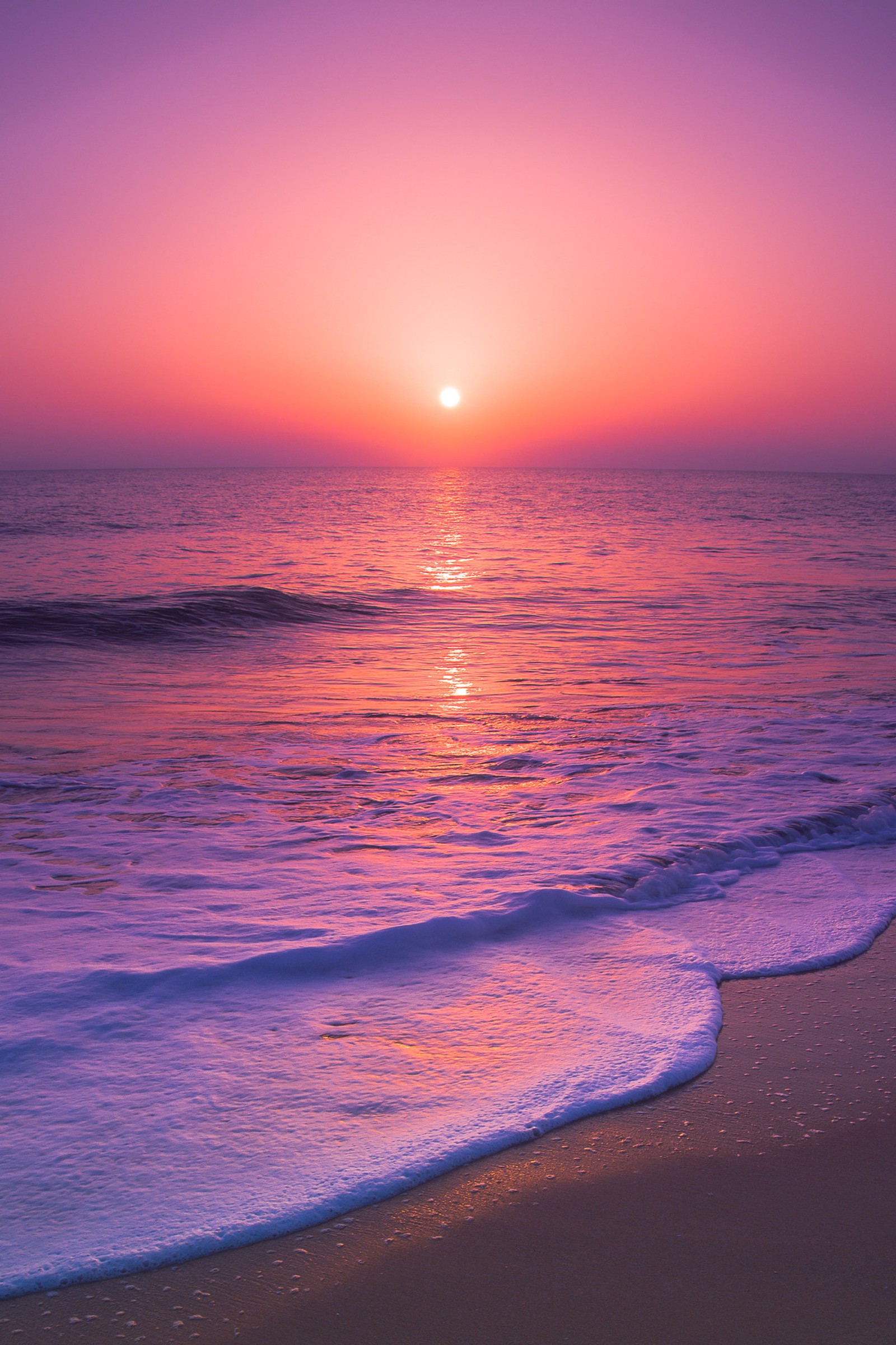 Un atardecer púrpura y naranja sobre el océano con olas entrando (playa, paisaje, amanecer, luz del sol, cielos)