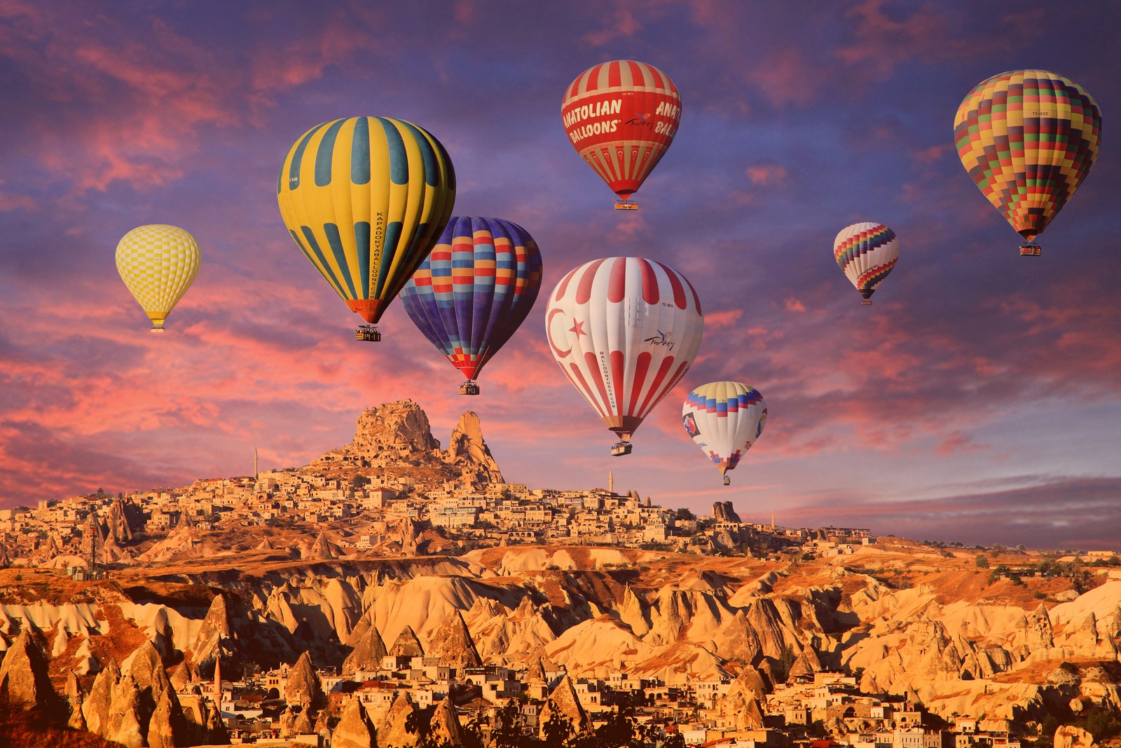 A group of hot air balloons flying over a rocky landscape (hot air balloons, cappadocia, golden hour, rock formations, town)