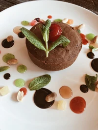 Postre de chocolate decadente adornado con menta y salsas coloridas, rodeado de coberturas vibrantes.