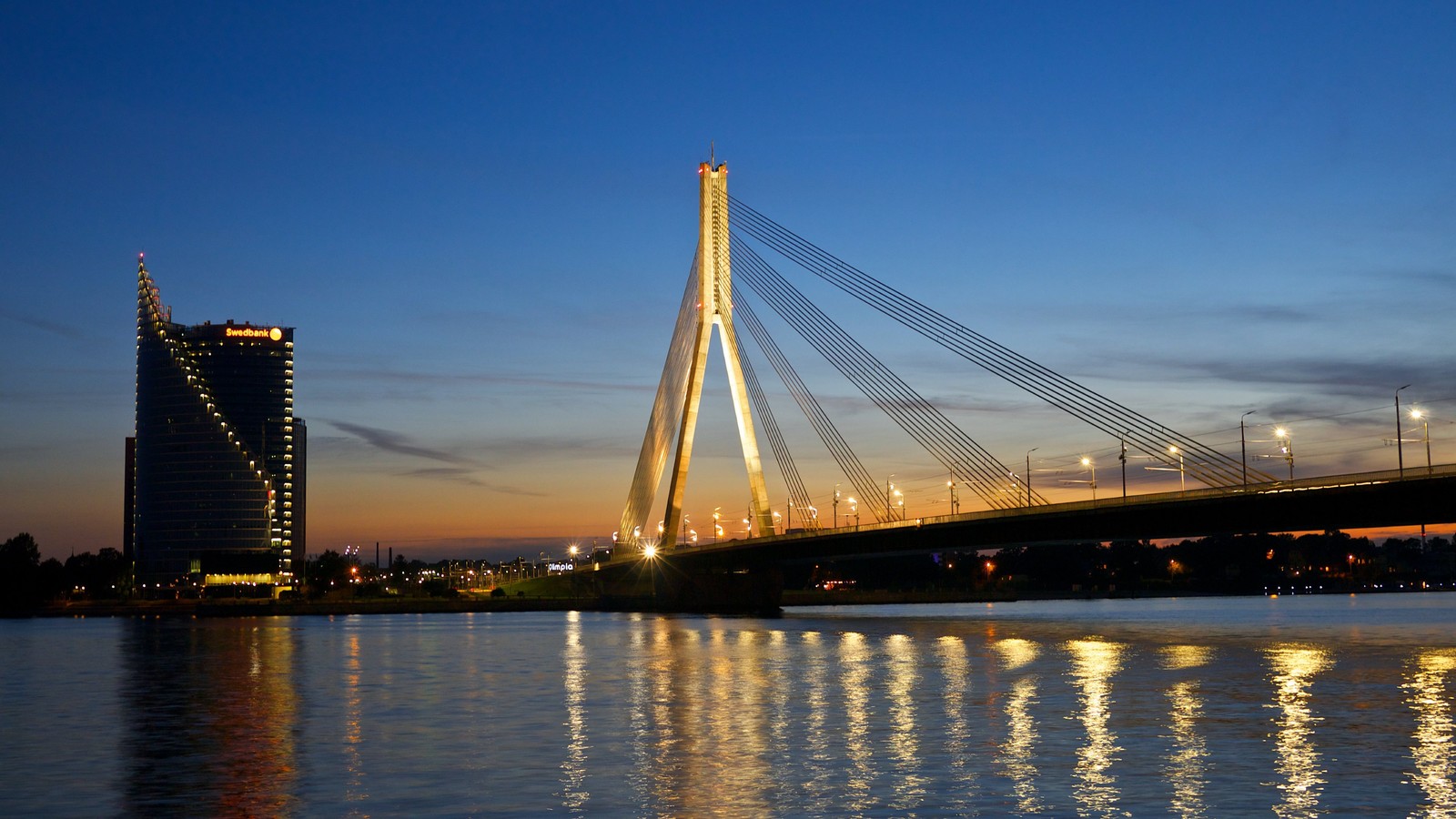 Uma ponte árabe sobre um corpo d'água com uma cidade ao fundo (riga, ponte estaiada, ponte, marco, reflexo)