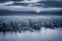 Monochrome Stadtlandschaft bei Dämmerung, die eine weitläufige Metropole mit Wolkenkratzern zeigt, die sich im Wasser spiegeln.