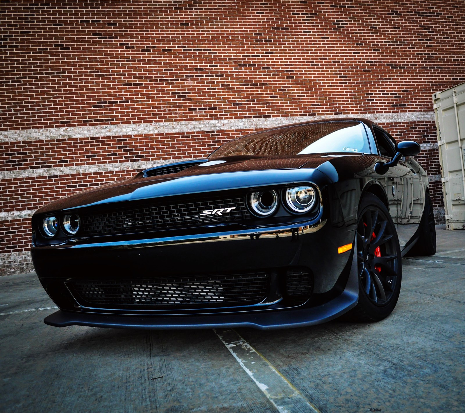 A close up of a black dodge car parked in front of a brick building (auto, car, challenger, dodge, hellcat)