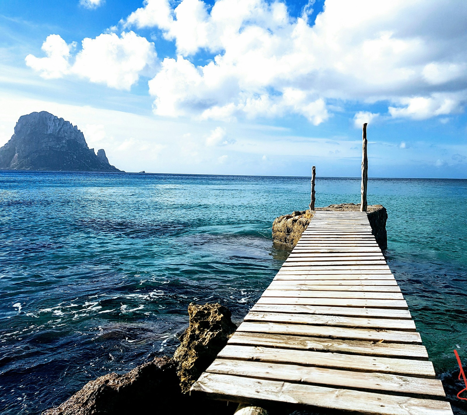 Um píer de madeira se estendendo para o oceano com uma montanha ao fundo (ibiza, mar, natureza, paisagem)