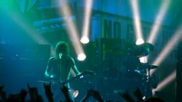 Dynamic rock concert performance with a guitarist and drummer illuminated by vibrant green stage lights, engaging an enthusiastic audience.