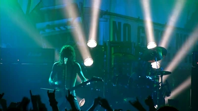 Dynamic rock concert performance with a guitarist and drummer illuminated by vibrant green stage lights, engaging an enthusiastic audience.