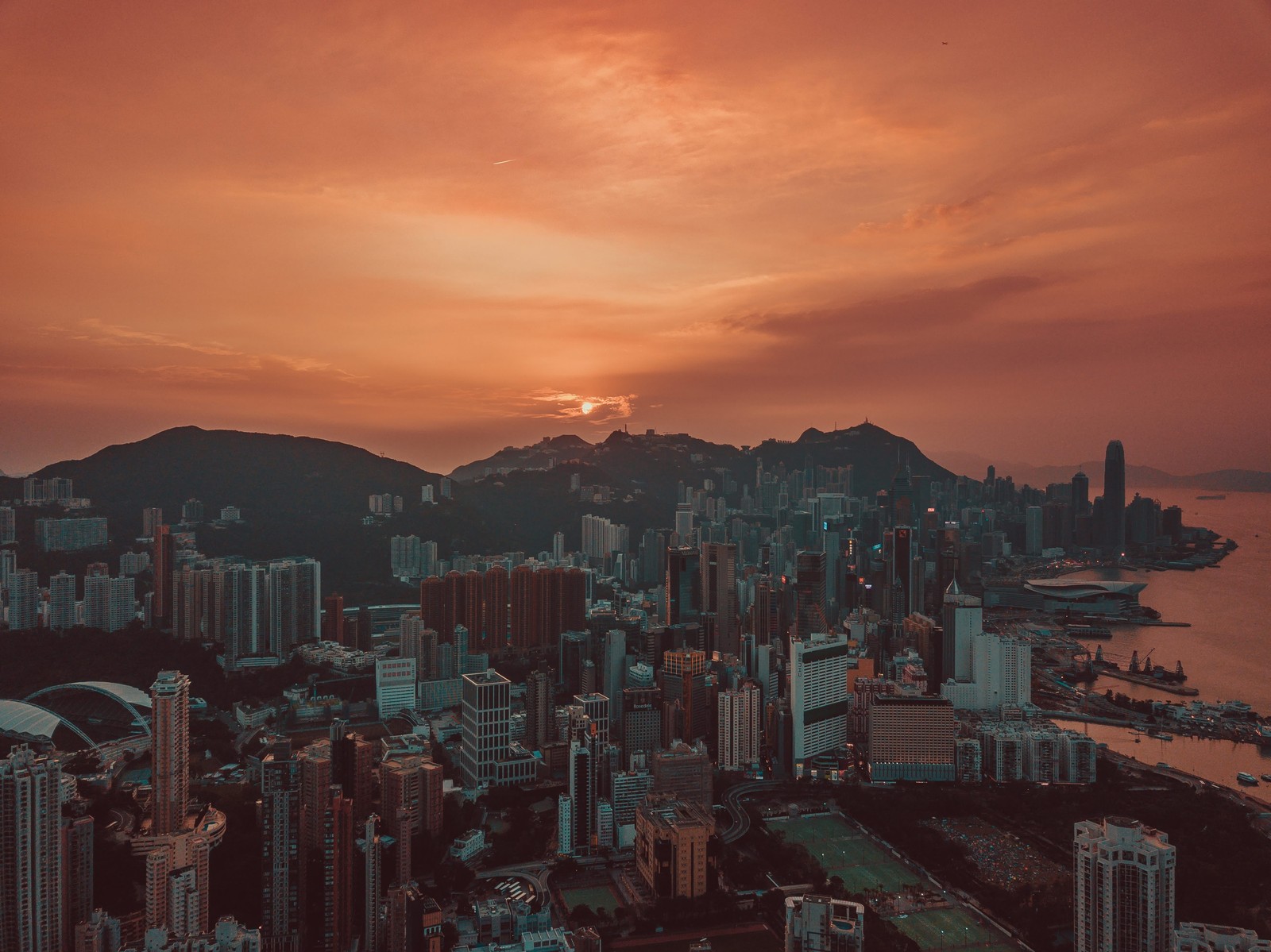 Vista aérea de uma cidade com um pôr do sol ao fundo (por do sol, hong kong, cidade, paisagem urbana, metrópole)