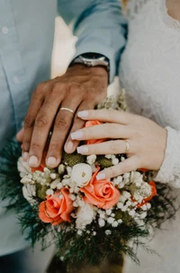 Manos unidas con anillos de boda y un vibrante ramo de flores