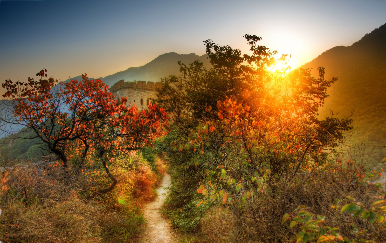 Una vista de un camino que lleva a una montaña con una puesta de sol (gran muralla china, naturaleza, luz solar, vegetación, mañana)