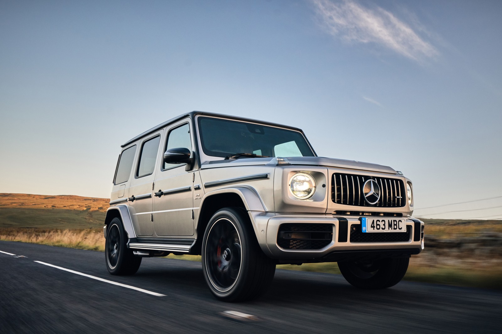 Um close-up de um mercedes g-class prateado dirigindo por uma estrada (carro, pneu automotivo, pneu, roda, mercedes benz g class)