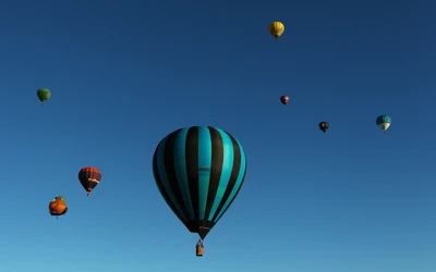 Bunte Heißluftballons schweben durch einen klaren blauen Himmel zwischen flauschigen weißen Wolken.