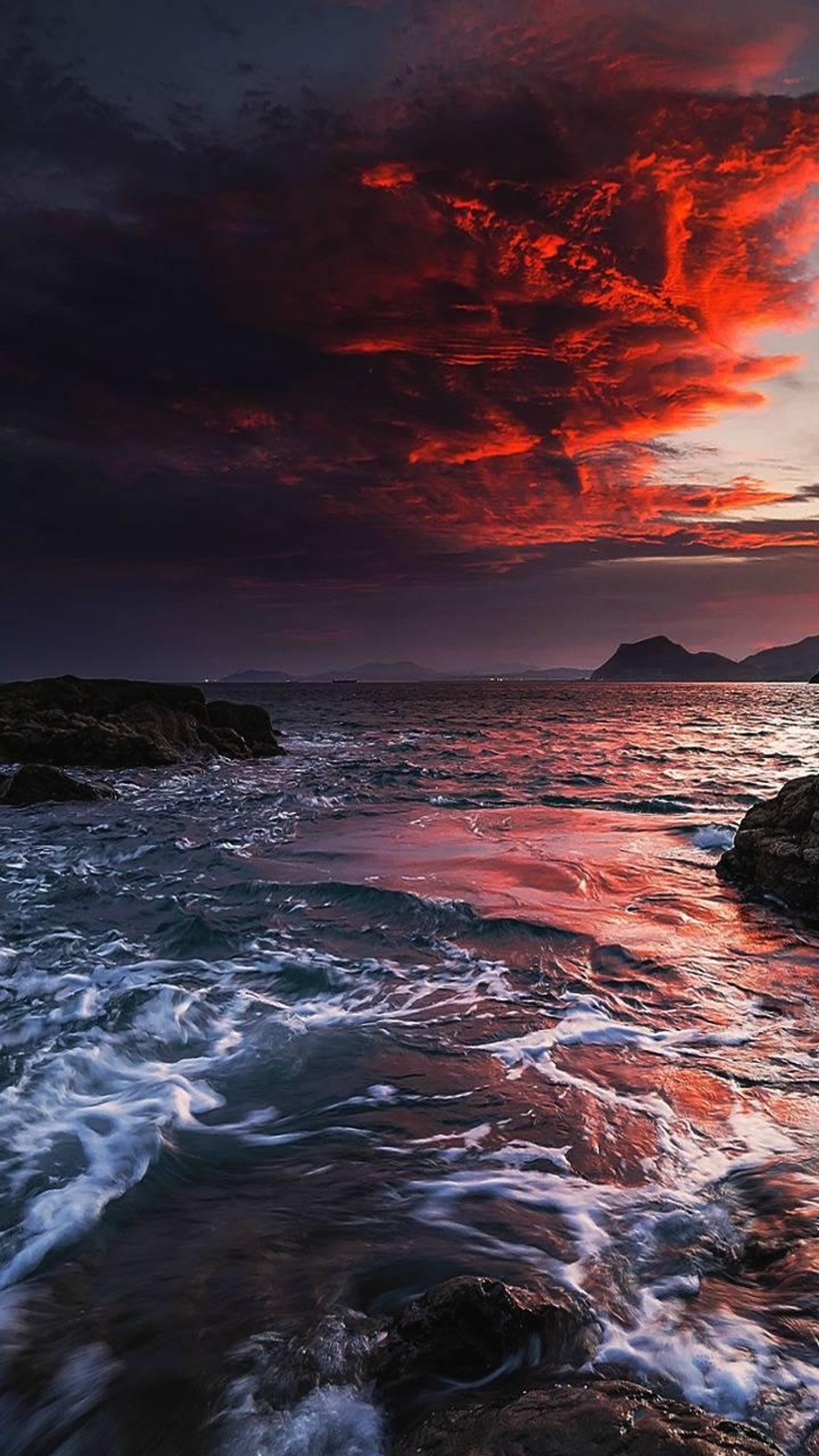 Sunset over the ocean with waves crashing in front of a rocky shore (ocean, sunset)