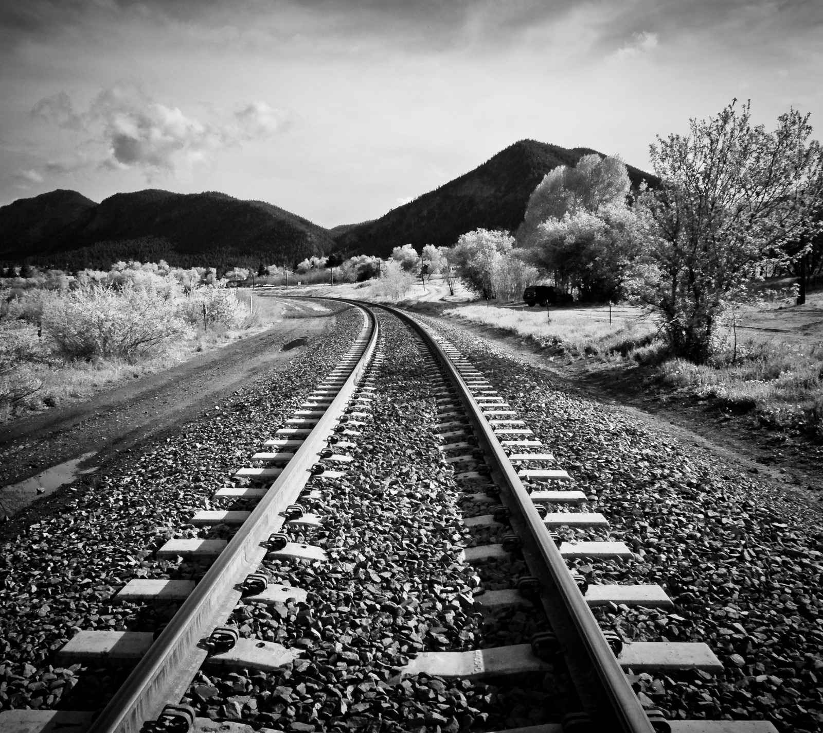 Una foto en blanco y negro de una vía de tren con montañas al fondo (negro, camino, blanco)