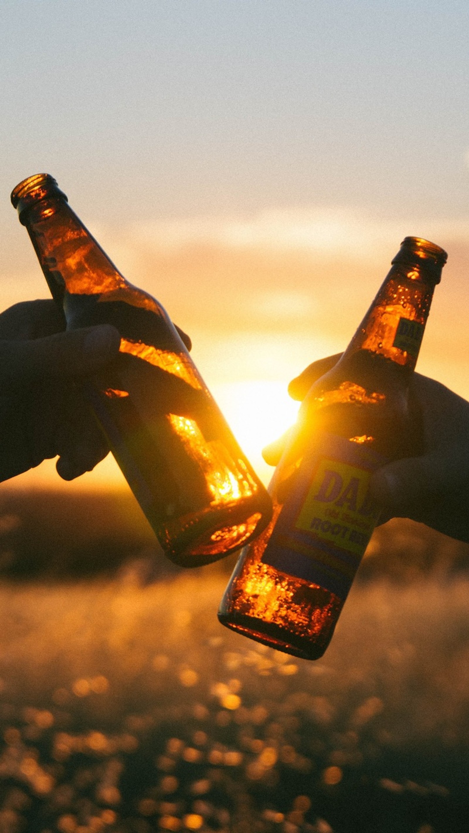 Jemand hält zwei bierflaschen in den händen mit der sonne, die hinter ihnen untergeht (bier, getränk)