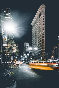 Paysage urbain nocturne avec un gratte-ciel historique, des lumières de rue vibrantes et un trafic flou dans un environnement urbain animé.