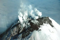 Stratovolcan en éruption entouré de nuages, présentant un paysage volcanique dramatique.