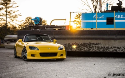 Honda S2000 jaune garé près d'un quai au coucher du soleil, mettant en valeur son design élégant et son profil sportif.