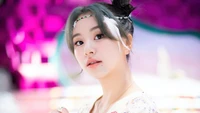 Chaeyoung do TWICE, exibindo uma expressão cativante com um penteado delicado e um fundo colorido.