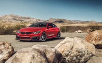 Carro esportivo BMW M4 vermelho em estrada desértica com paisagem rochosa