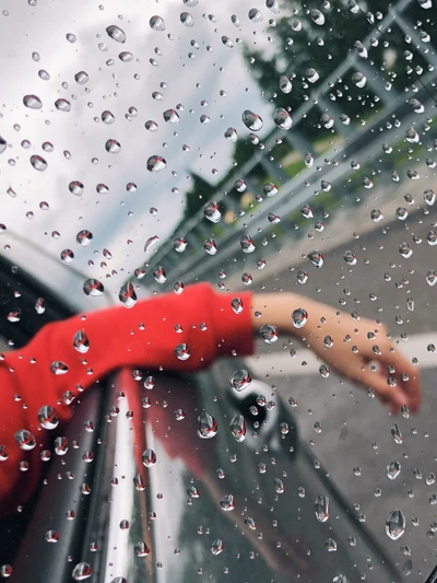 Gotas de chuva em uma janela de carro com uma mão descansando do lado de fora, capturando um momento de tranquilidade em meio a uma garoa.