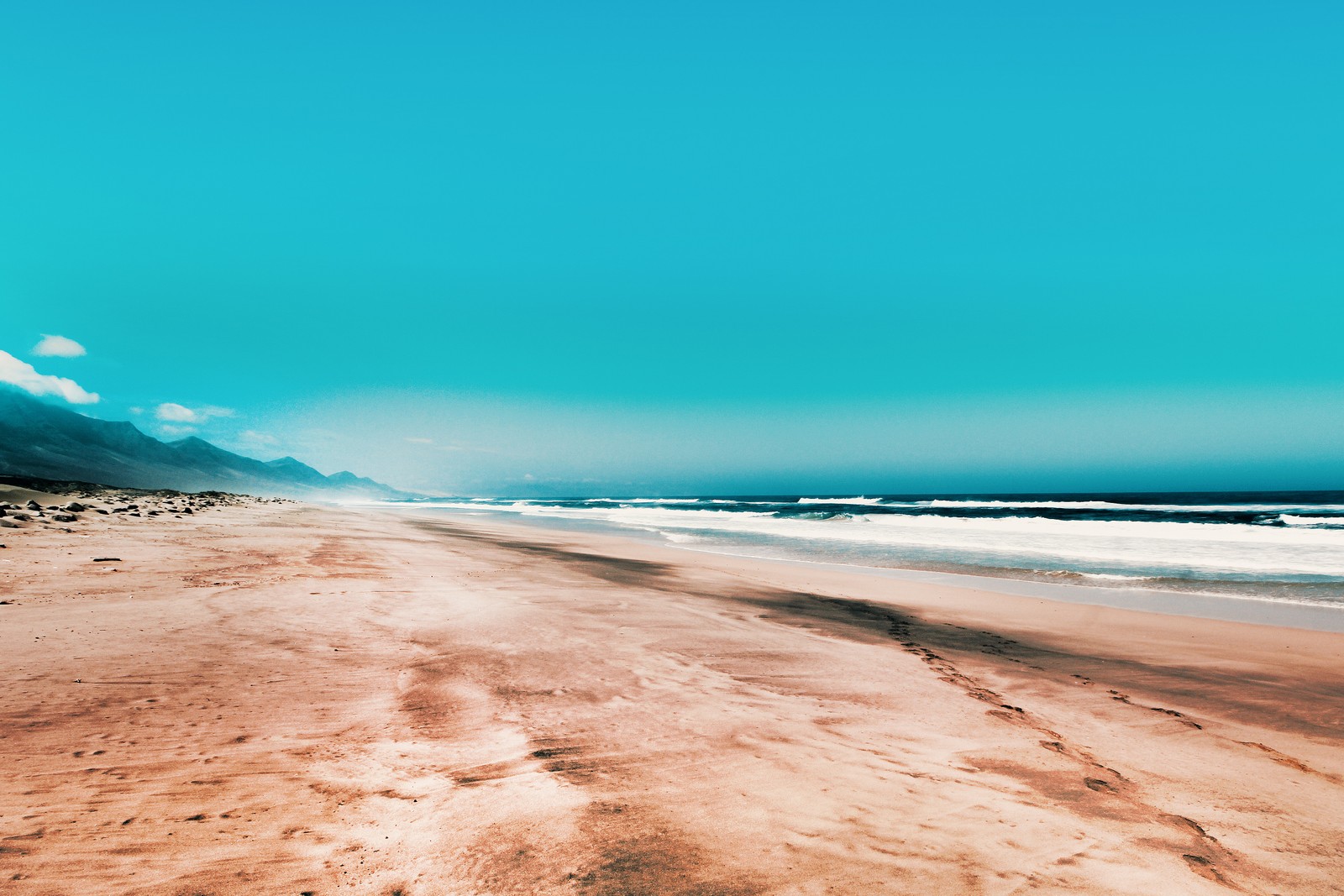 Vista de uma praia com algumas pegadas na areia (praia, costa, areia, azul, mar)