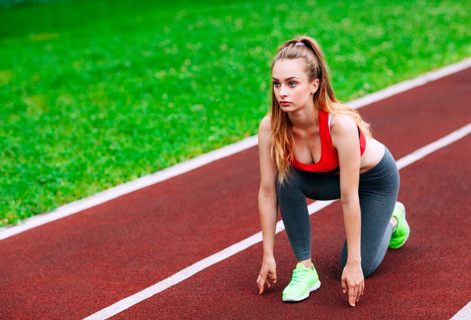 Une femme en haut rouge et pantalon gris accroupie sur une piste (course, athlète, sports, athlétisme, lieu sportif)