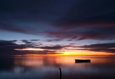 Horizonte sereno: Reflexión tranquila del atardecer con bote en silueta