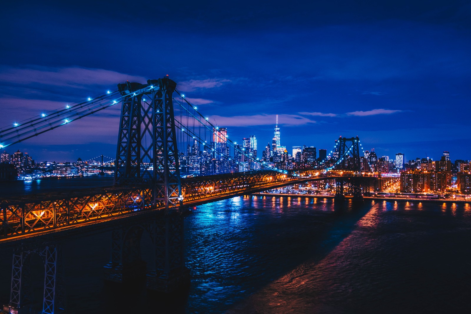 Vista de un puente sobre un río con una ciudad al fondo (puente de williamsburg, puente colgante, nueva york, new york city, luces de la ciudad)