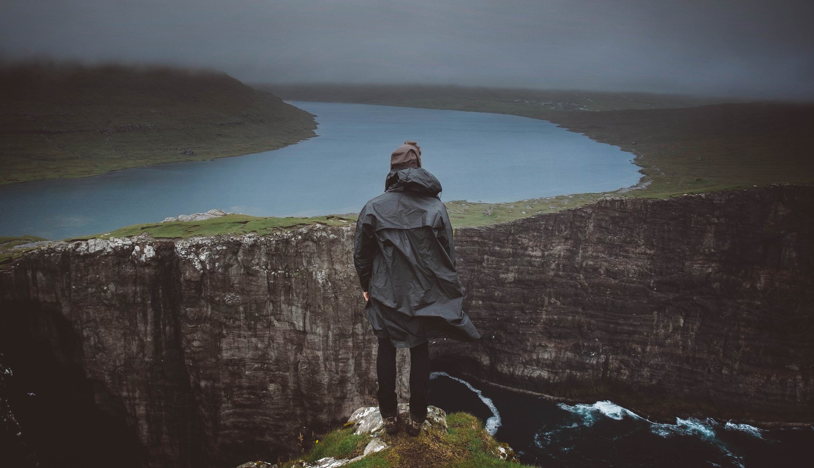 Un homme se tenant sur une falaise regardant un lac et une falaise (eau, mer, la côte, hauts plateaux, falaise)