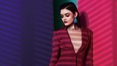 Lucy Hale dans un costume bordeaux élégant devant un fond rayé vibrant.